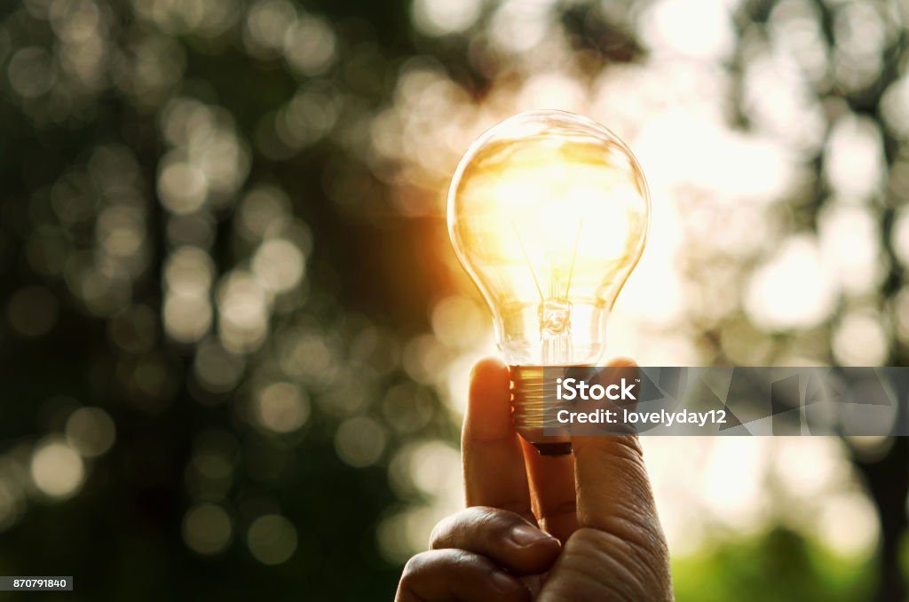 lampadina a mano e tramonto in natura, concetto di energia elettrica - Foto stock royalty-free di Lampadina