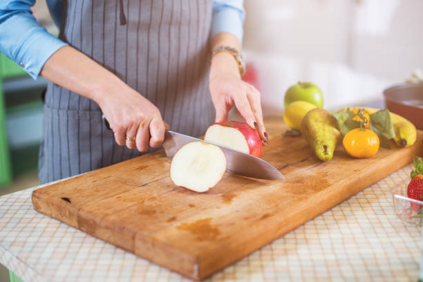 istock Hands cutting an apple on chopping board. Young woman preparing a fruit salad in her kitchen 870799414