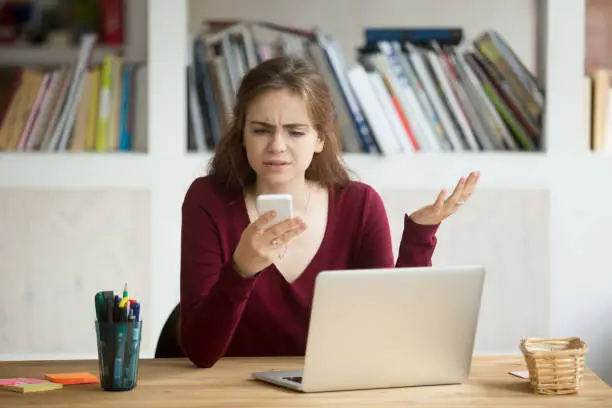 Photo of Frustrated female entrepreneur looking at cellphone and shrugging.