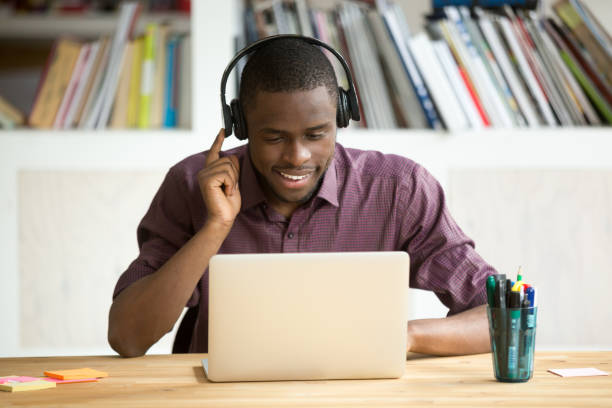 Casual smiling office worker in headphones looking at laptop screen.