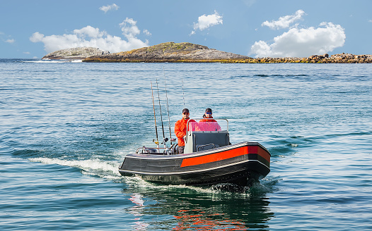 Two fishermen sail on a motor boat by sea against the background of the island. Float directly to the camera