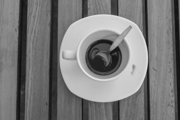 Abstract black and white image dirty coffee cup and spoon setting on white saucer and wooden table after drinking in the morning. (Soft focus)