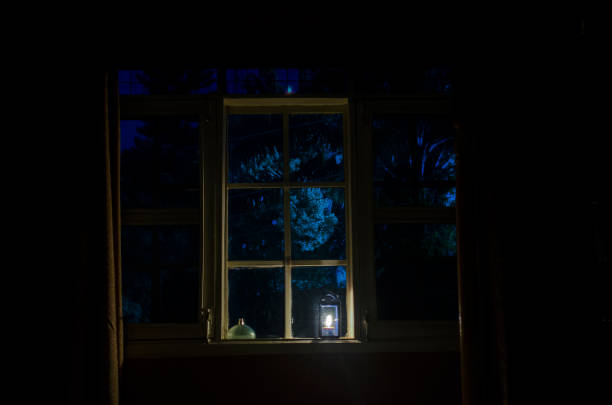 A candle illuminates a bedroom window from the inside of the room. A candle illuminates a bedroom window from the inside at twilight, while the blue sky is seen through the window creating a blue tint effect on the window. low lighting stock pictures, royalty-free photos & images