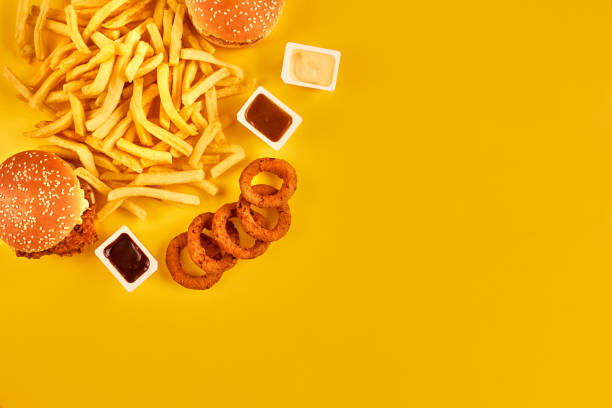 Fast food concept with greasy fried restaurant take out as onion rings, burger, fried chicken and french fries as a symbol of diet temptation resulting in unhealthy nutrition