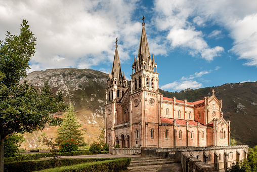 Basilica of Santa Maria la Real de Covadonga, Asturias, Spain, Europe. Beautiful church of touristic travel destination in autumn with a vibrant colorful sky and green natural forest with mountains.