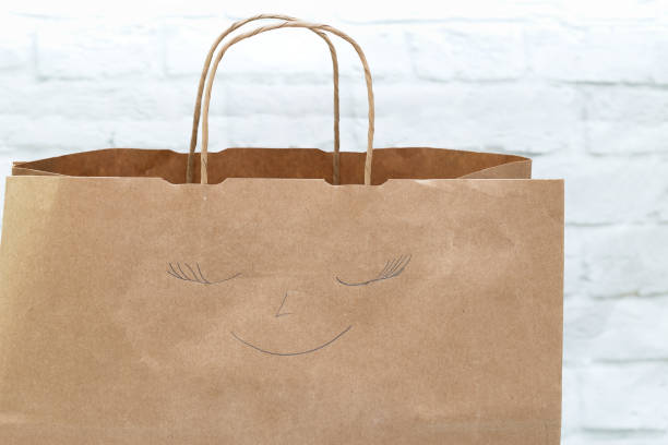 istock Paper shopping bag with a smile painted on a white brick wall background 870860366