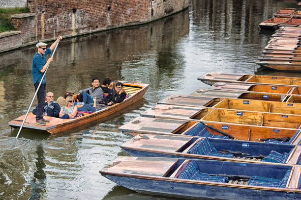 Punting on the River Cam A group of tourists of mixed ethnicity on a punt on the River Cam in Cambridge, England. Cambridge is famous for punts and is one of the two premiere University towns in the UK. This is being punted by an official tour guide as part of a rental package. couple punting stock pictures, royalty-free photos & images