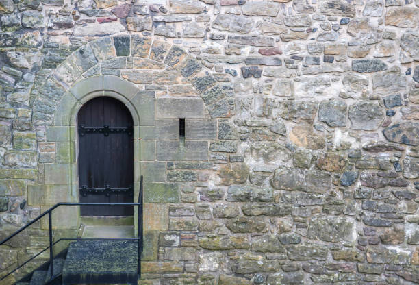 Single Arched Wooden Door stands in contrast to stones in ancient wall of varying sizes and shapes.