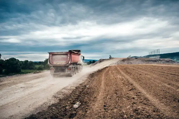 Photo of Industrial dumper trucks working on highway construction site, loading and unloading gravel and earth.