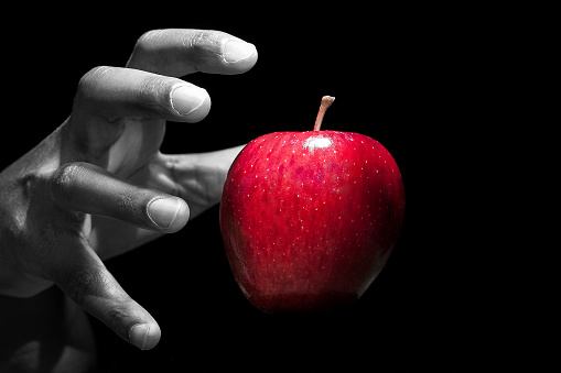 Here is a black and white picture of a person reaching for a red apple