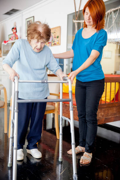 istock Assistant in Retirement Home Helping Senior Woman Walking with Mobility Walker 870909560