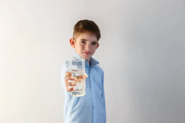 Boy holds a glass of water on a light background. Focus on a glass of water. Copy space