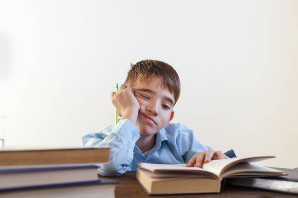 istock Schoolchild sits at a table and reads the book. Does homework. On a light background 870919092