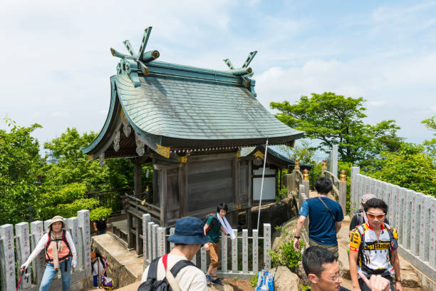Small group of Japanese tourists hiking on Shirakumobashi trail on Mount Tsukuba, they stop at small temple on the top, Japan
