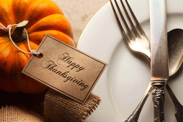 istock Happy Thanksgiving Tag Tied To Small Pumpkin Next To Place Setting 870930666