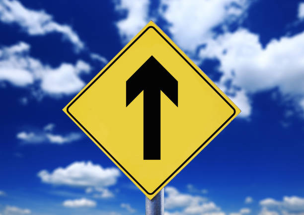 istock Yellow road sign with cloudscape with arrow symbol 870935122