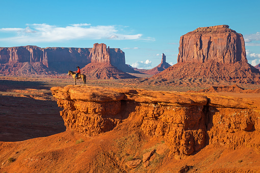 The John Ford's viewpoint inside the Monument Valley Navajo Tribal Park with a Navajo Horseman staging the scene of the movie Stagecoach at sunset, Arizona, USA.