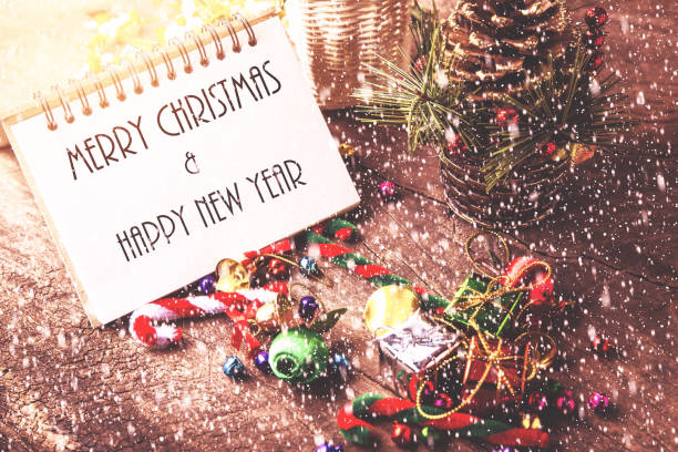istock Merry christmas and Happynew year text on blank notebook with snow, gift box, daisy flower, candy ball and cane pine decoration on vintage wooden background. 870968640