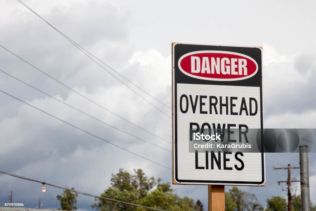 Danger overhead power lines sign Danger overhead power lines sign with overcast sky and power lines Power Line Stock Photo