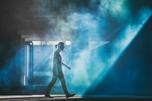 A mysterious man walking through the blue smoke towards the shadow