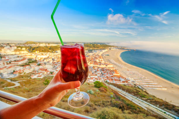 Glass of Sangria in woman hand on Nazare skyline background. Holiday concept and celebration. Lifestyle aperitif in Nazare Sitio, Portugal's famous tourist resort on the Atlantic coast.