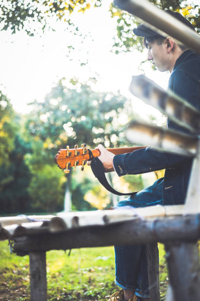 young man playing guitar on park bench.