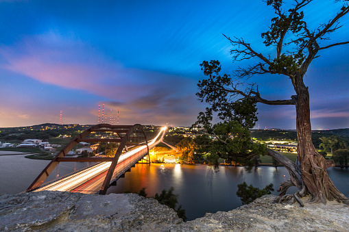 This is a wide angle long exposure show of the Pennybacker 360 Bridge in Austin Texas. On the left the bridge with stream lighting traffic, and on the left a well lit tree. Wide enough to see the long Colorado River and beautiful colors in the sky. Taken with Canon 70D & 10-18mm f/4.5 lens.