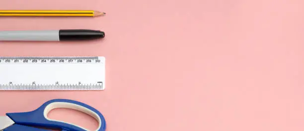 Banner image of office supplies and tools including a pair of scissors, a plastic ruler, a marker pen, and pencil on pink backdrop with copy space