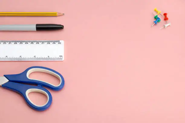 Office supplies and tools including scissors, ruler, pencil, marker pen, and push pins on a pink background with copy space