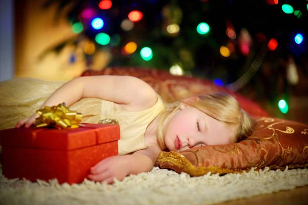 istock Adorable little girl sleeping under the Christmas tree by a fireplace 871041114