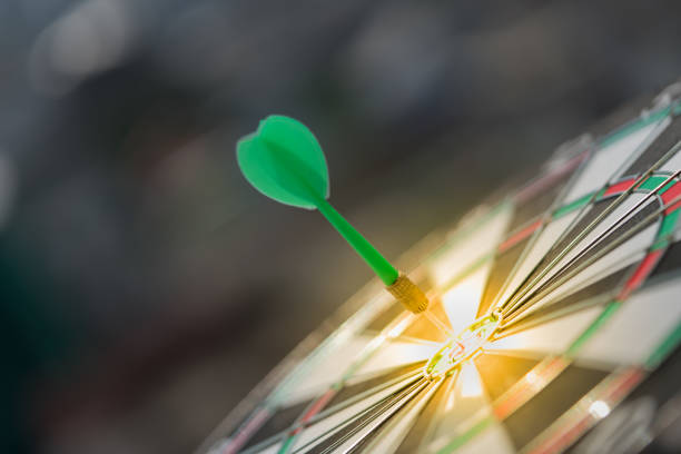 dart verde flecha golpea en el centro de diana de dardos con fondo puesta del sol y ciudad moderna - dartboard darts arrow sign target fotografías e imágenes de stock