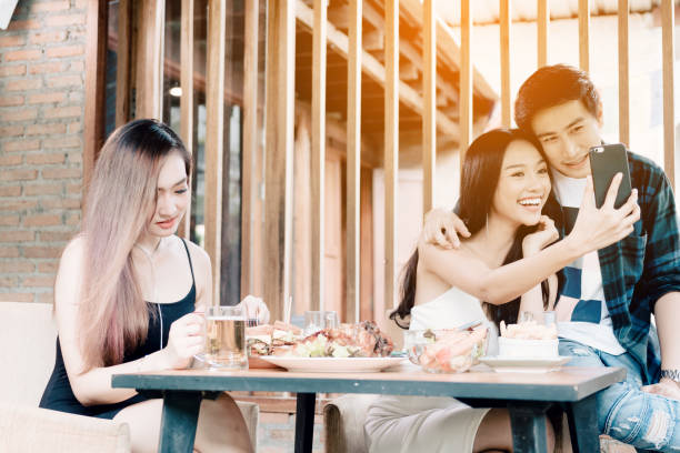 Asian single woman envious with love couple doing take selfie at restaurant. Asian single woman envious with love couple doing take selfie at restaurant. jealous ex girlfriend stock pictures, royalty-free photos & images