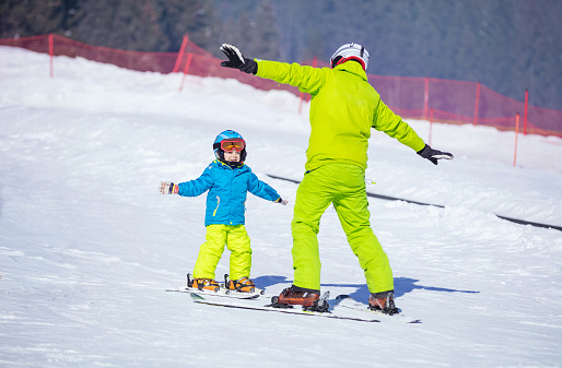 Lesson at skiing school: instructor teaching little skier how to make turns, young boy doing exercise on slope in children's area