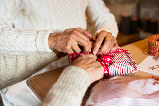 istock Unrecognizable senior couple in sweaters wrapping Christmas gift. 871091032