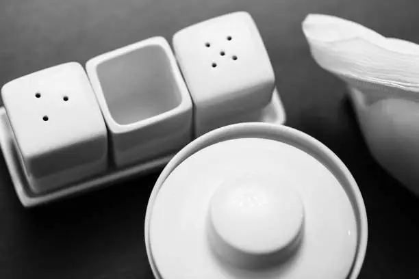 Black and white image of salt and pepper shakers, sugar-bowl and paper napkin holder in the wooden table