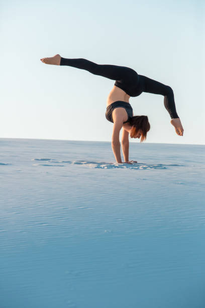 istock Young woman practicing inversion balancing yoga pose handstand on sand 871105316
