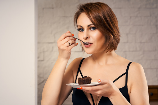 Attractive woman eating chocolate cake at home on couch