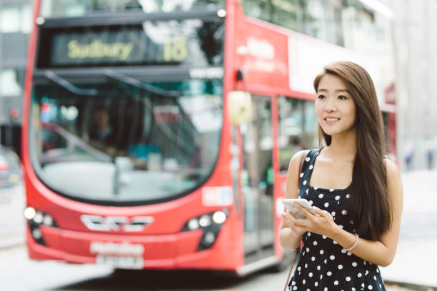 istock Young Woman Using Phone with Double Decker in Background 871124386