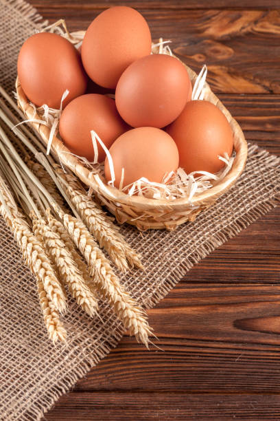 istock Chicken eggs horizontal banner. Eco farming concept. Red eggs and wheat ears on piece of sacking on brown wooden textured background. Organic food. 871125906