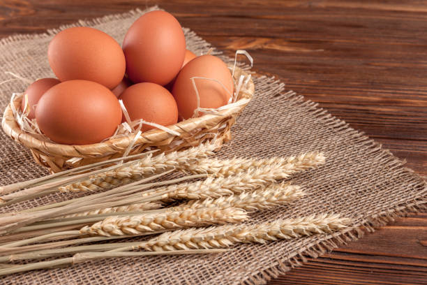istock Chicken eggs horizontal banner. Eco farming concept. Red eggs and wheat ears on piece of sacking on brown wooden textured background. Organic food. 871125936