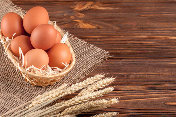 istock Chicken eggs horizontal banner. Eco farming concept. Red eggs and wheat ears on piece of sacking on brown wooden textured background. Organic food. 871125942