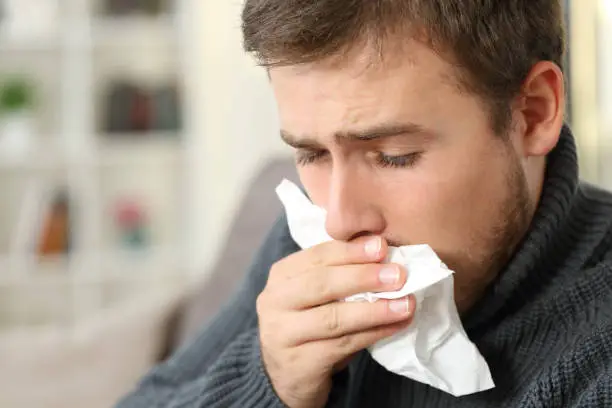 Photo of Man coughing covering mouth with a tissue at home