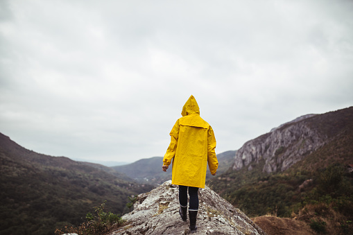 One woman, walking on mountain on a rainy day in yellow raincoat, rear view.