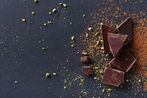 pezzi di cioccolato rotti e cacao in polvere su sfondo nero - brown chocolate candy bar close up foto e immagini stock