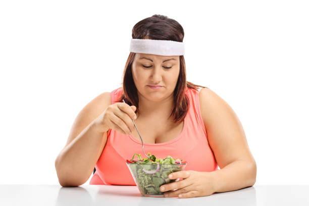 mulher com sobrepeso triste sentado em uma mesa e olhando para uma tigela de salada - overweight women salad frustration - fotografias e filmes do acervo