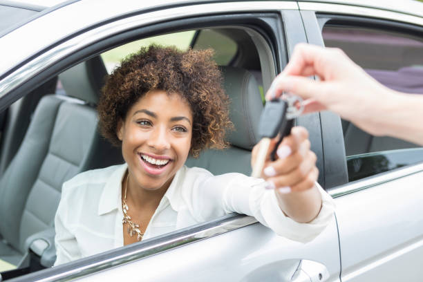 Excited young woman accepts new car keys An excited young woman smiles as she reaches from the driver's seat of her new car for her car keys.  Only the hand of her car dealer can be seen giving her the keys. car key photos stock pictures, royalty-free photos & images