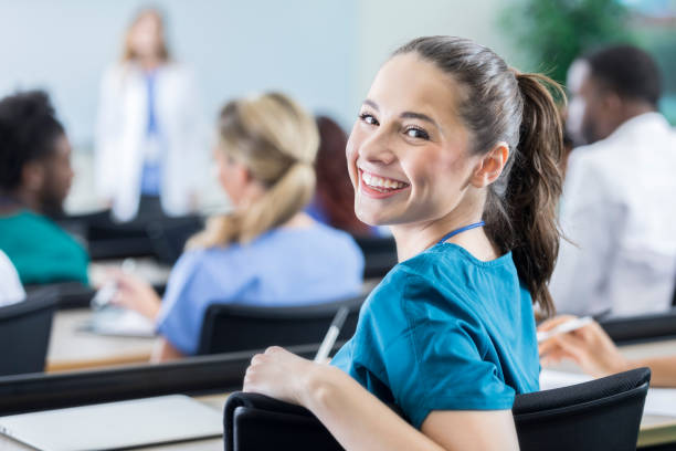 Cheerful female medical student in the classroom Beautiful young Hispanic female medical student smiles over her shoulder while attending class. medical education stock pictures, royalty-free photos & images
