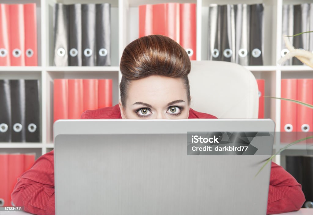 Business woman afraid and hiding behind the computer Business woman afraid and hiding behind the computer in office Adult Stock Photo