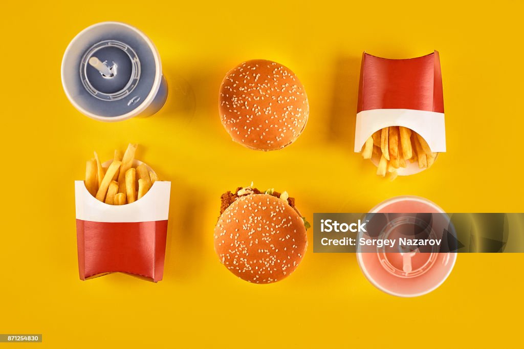 Fast food and unhealthy eating concept - close up of fast food snacks and cold drink on yellow background Fast food and unhealthy eating concept - close up of fast food snacks and cold drink on yellow background. Top view. Copy space. Still life. Flat lay. Fast Food Restaurant Stock Photo