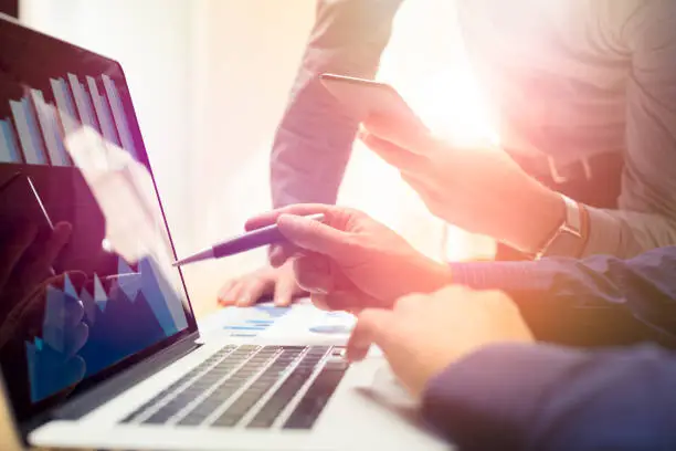 Photo of Two colleagues working on new global financial strategy plan using laptop and smartphone.Modern business team innovation concept.Project meeting at office with virtual graph and chart data interface